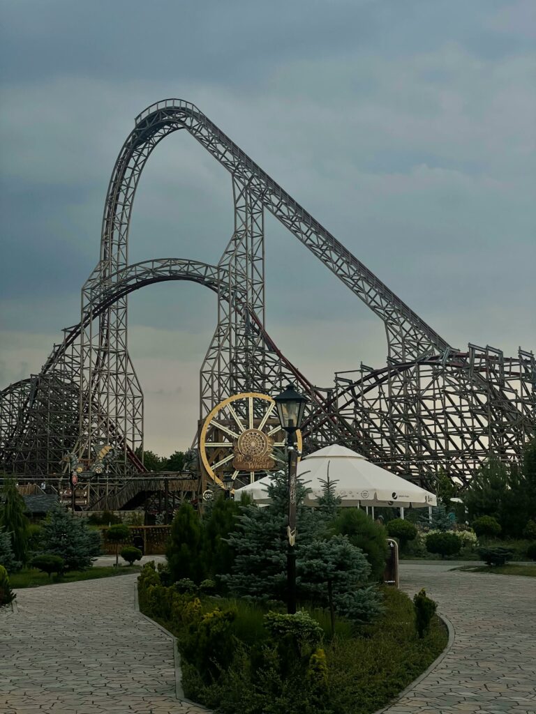 Impressive steel roller coaster in Energylandia, Zator, Poland with lush greenery and cloudy sky.